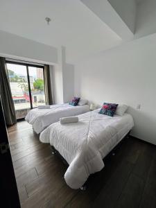 two beds in a white room with a window at Apartamento con Piscina de 2 habitaciones Edificio Brunelo Ciudad de Guatemala, Céntrico in Estación Pamplona