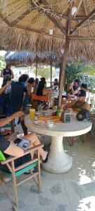 a group of people sitting at tables under a straw umbrella at Hostal Pelikan Taganga in Taganga