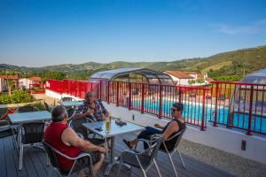 drie mensen zitten aan een tafel op een terras met een zwembad bij Domaine Chalets Larlapean in Saint-Martin-dʼArrossa