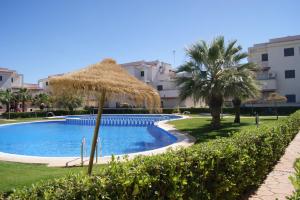 a swimming pool with a straw umbrella and palm trees at Marineu Las Arenas in Alcossebre