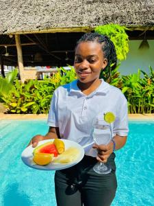 a woman holding a plate of fruit and a glass of wine at Lala salama Kendwa villas in Kendwa