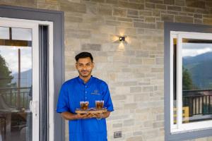 un homme tenant un plateau avec deux verres de bière dans l'établissement SaffronStays The Mountain Escape, à Mukteswar