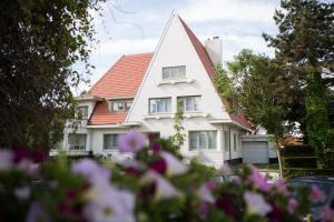 a white house with a red roof and some flowers at Villa Emilia in De Haan