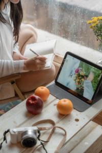 a woman sitting at a table with a tablet and fruit at Happy Town Tà Xùa - Thị Trấn Vui Vẻ in Bắc Yên