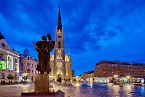 eine Statue vor einem Gebäude mit einem Uhrturm in der Unterkunft Apartments Center HSV in Novi Sad