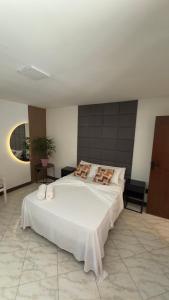une chambre avec un grand lit avec des draps et des oreillers blancs dans l'établissement Flats do Cabo e Suítes, à Arraial do Cabo