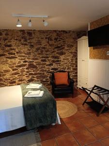 a bedroom with a bed and a chair and a stone wall at Nuevo sabor rural Ribeira Sacra in A Pobra do Brollon +14 photos
