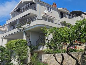 a white apartment building with balconies and trees at Apartmani Marinović in Podgora