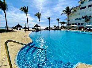 a large swimming pool next to a beach with palm trees at FRENTE AL MAR A PIE DE PLAYA ALBERCA y JACUZZI in Mazatlán