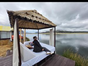 a woman sitting on a bed on a dock with a umbrella at KAY PACHA LODGE Uros in Puno +7 photos