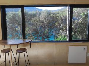 a table and two stools in front of a large window at Haven Cabin - No road access - just a boat ride away in Endeavour Inlet