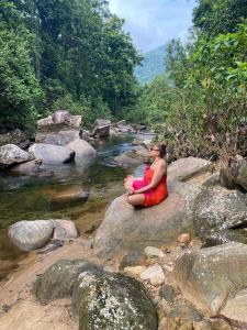 a woman sitting on a rock next to a river at komalie resort in Kitulgala