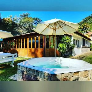 a hot tub with an umbrella in front of a house at Paraíso aconchegante em Itaipava in Itaipava