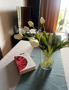 a vase with white flowers and a book on a table at EUROPA22 "Hostel - prywatne 3 pokoje" lub "Apartament cały z 3 pokojami" - CENTRUM MIASTA Szybkie i Łatwe Zameldowanie 24h in Tomaszów Mazowiecki