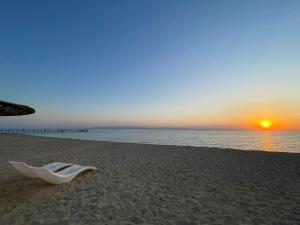 a white chair sitting on a beach with the sunset at White Bay Ras Sedr وايت باي راس سدر in Ras Sedr