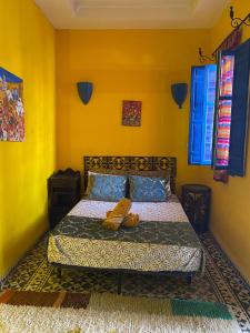 a bedroom with a bed with yellow walls and blue windows at Riad Safi médina in Safi