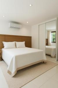 a bedroom with a large white bed and a mirror at La Petite Suisse - Condomínio Charmoso em Imbassaí in Mata de Sao Joao