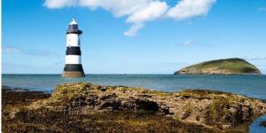 a lighthouse on the ocean with a rock in the foreground at Cozy bell tent with heating and smart Tv in Llanfairpwllgwyngyll +11 photos