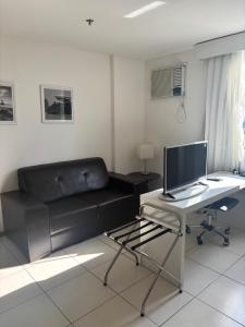 a living room with a black couch and a desk with a computer at Flat Aconchegante in Campos dos Goytacazes