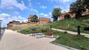 a sidewalk with two benches and a castle in the background at Apartament u Krzyżaka in Malbork