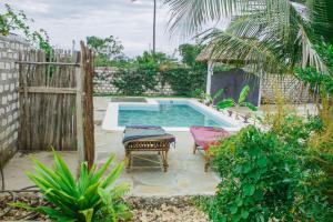 a pool with two chairs and a table and a fence at Red Land House in Watamu