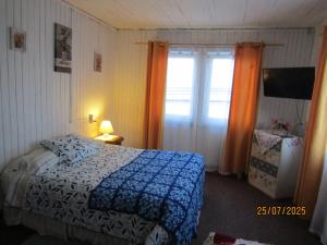 a bedroom with a bed with a blue comforter and a window at Hostal Casa del Tiempo in Quellón +13 photos