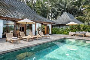 ウブドにある1BRV Cozy Villa with Amazing Rice Paddy Viewの家の隣にある椅子とパラソルのあるプール