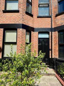 a brick building with a black door and a bush at 4 Bedroom Belfast Townhouse in Belfast