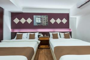 two beds in a room with a purple wall at Hotel Grand Orchard in Gua Sai