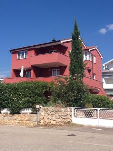 um edifício vermelho com uma árvore em frente em Apartments Mare em Punat