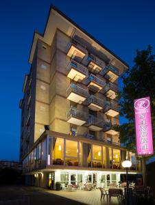 Um edifício alto com um letreiro cor-de-rosa à frente. em Hotel Sandra em Rimini