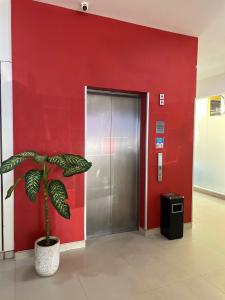 a plant in front of a red wall with a elevator at Alltrue Lite Hotel Nagoya Hill Batam in Nagoya