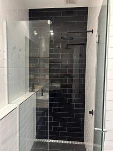 een douche met zwarte tegels en een glazen deur bij THE DEVLIN APARTMENTS 2 Bedroom Apartment near GMHBA stadium in Geelong - G04 in Geelong +8 foto's