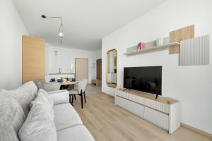 a white living room with a couch and a tv at Lets Sea Baltic Park by Solarento in Gąski