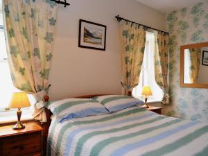 a bedroom with a bed and two windows with curtains at Gable Cottage in Keswick