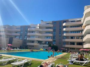 a pool in front of a large building with people sitting in chairs at Mindelo apart in front of the best beach of North Portugal in Mindelo
