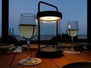 a table with two glasses of white wine and a lamp at Elysian Bay Cottage in Boggomsbaai +11 photos