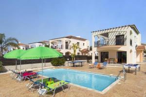 a swimming pool with chairs and umbrellas next to a house at Villa Kassiopeia by Villa Plus in Peyia