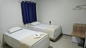 two beds in a room with blue curtains at Hotel Moriah in Umuarama