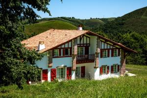 une maison blanche avec des fenêtres rouges et une colline dans l'établissement Auberge Ostapé, à Bidarray