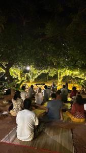 un gruppo di persone sedute a terra sotto un albero di HostelExp, Auroville - A Rural Retreat Experience ad Auroville
