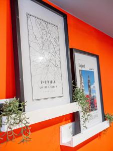 two framed pictures on an orange wall with plants at City Center Studio Apartments By AVO Apartments Sheffield in Sheffield