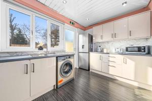una cucina con mobili bianchi, lavatrice e asciugatrice di Quirky, Family Home in Glasgow a Cardonald