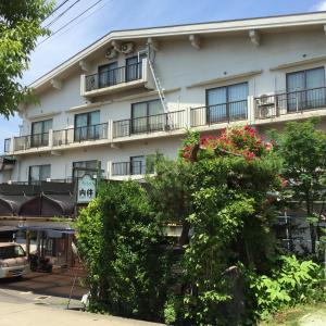 biały budynek z balkonami i czerwonymi kwiatami przed nim w obiekcie Uchihan w mieście Nozawa Onsen