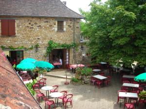 un patio al aire libre con mesas, sillas y sombrillas en Hôtel Chastrusse en Nadaillac-de-Rouge