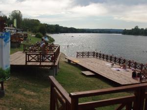 a dock on a lake with people sitting on the grass at Nobus Vila jezero in Veliko Gradište +4 photos