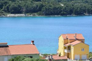 ein gelbes Haus mit roten Dächern neben dem Wasser in der Unterkunft Apartments Buturi in Soline