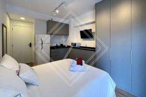 a bedroom with a white bed and a kitchen at Zainalofts7Vila Mariana ao lado metrô, CASV 117 ID in Sao Paulo