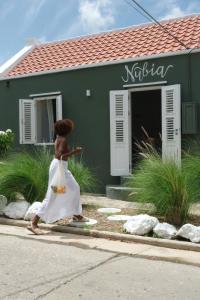 Una mujer con un vestido blanco caminando delante de una casa en Nubia Suites - Boutique luxury appartments in Otrobanda - UNESCO area, en Willemstad