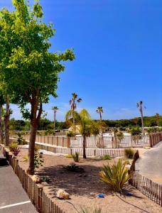 a fence with trees and palm trees behind it at Mobil-home domaine la yole 5 étoiles in Vendres